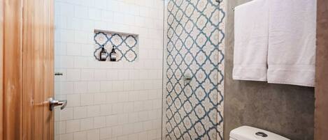 Un baño con ducha, inodoro y lavamanos con un rebozo de azulejos estampados.