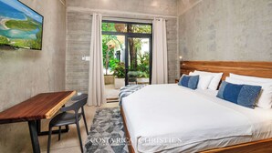 Ein Schlafzimmer mit einem großen Bett, einem Holztisch und Blick auf einen Garten durch eine Glastür.