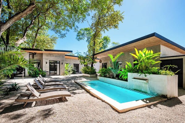 A modern house with a swimming pool, outdoor seating, and lush greenery.
