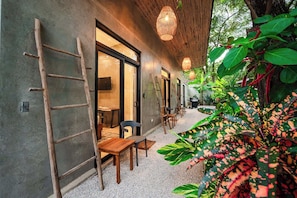 A modern outdoor seating area with tables and chairs, a wooden ladder, and lush greenery.