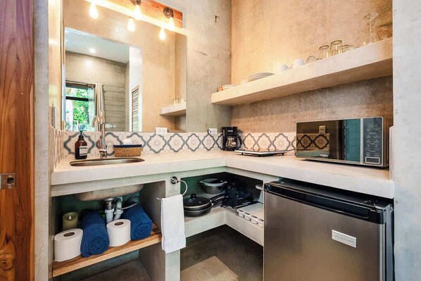 A compact kitchen with a microwave, stove, and refrigerator, a small window, and a mirror above the sink.