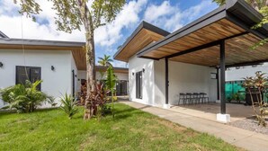 Una casa moderna de dos pisos con un porche cubierto, un pequeño jardín con palmeras y un cielo despejado.