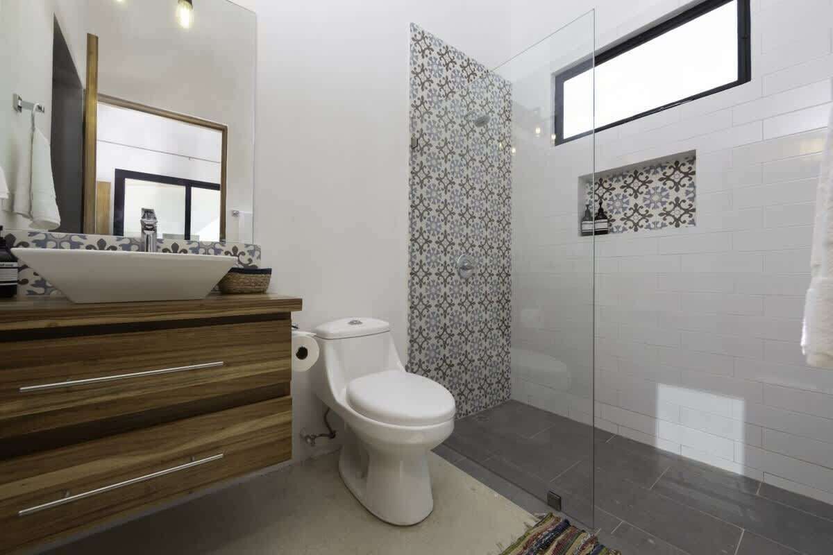 Un bagno moderno con un mobile vanitario in legno, un water bianco, box doccia in vetro e piastrelle decorate.
