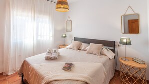 A neatly arranged bedroom with a bed, pillows, a bedside lamp, a small table, and a mirror on the wall. - Casa Mati Cómpeta by Ruralidays (Málaga)