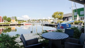 Un puerto deportivo con barcos amarrados, una mesa con sillas y vistas a edificios y árboles.