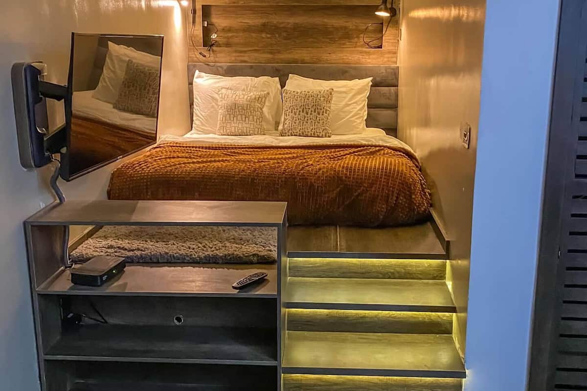 Un dormitorio moderno con una cama, un espejo, un televisor y una escalera.