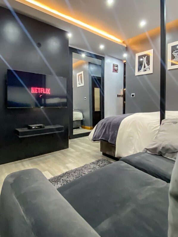 Une chambre d’hôtel moderne équipée d’un téléviseur à écran plat affichant « NETFLIX », d’un lit, d’un canapé et d’un miroir qui reflète la pièce.