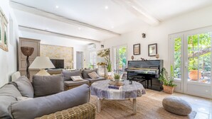 A spacious living room with a grey sofa, a piano, and a large window with a view of greenery. - Provencal bastide with heated pool near Alpilles and Luberon (Vernègues)