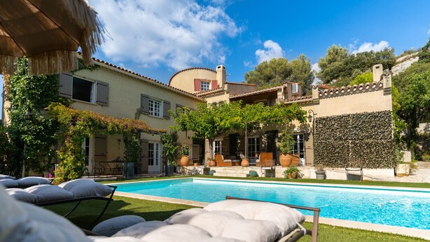 A poolside area with lounge chairs, a swimming pool, and a building with a tiled roof and greenery. - Provencal bastide with heated pool near Alpilles and Luberon (Vernègues)