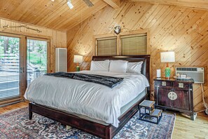 A wooden-paneled bedroom with a large bed, two bedside lamps, a vintage radio, and a window with blinds.