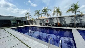 A swimming pool with a clear blue water surface, surrounded by a tiled deck and palm trees. - Blue Apple Hotel (Lekki)