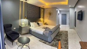 A modern bedroom with a large bed, a bedside table, a chair, and a small round table. - Blue Apple Hotel (Lekki)