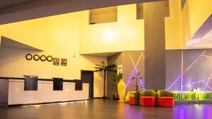 A modern reception area with a reception desk, a large plant, and colorful geometric lighting. - Blue Apple Hotel (Lekki)