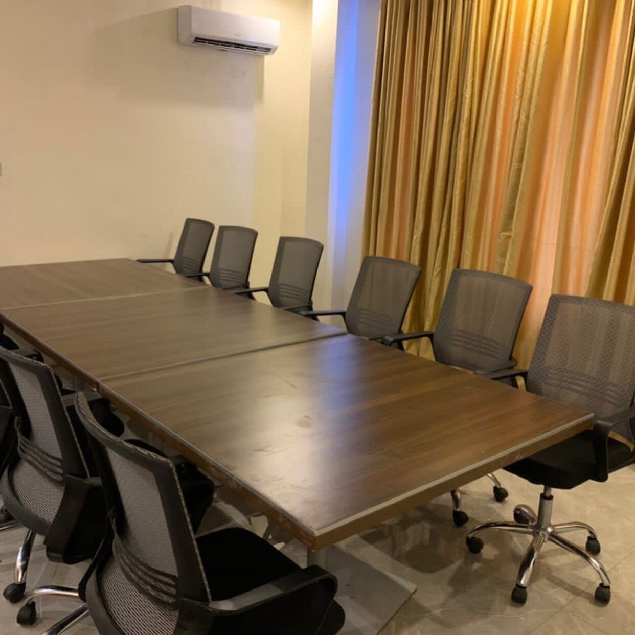 A conference room with a long table, six chairs, and an air conditioning unit on the wall.