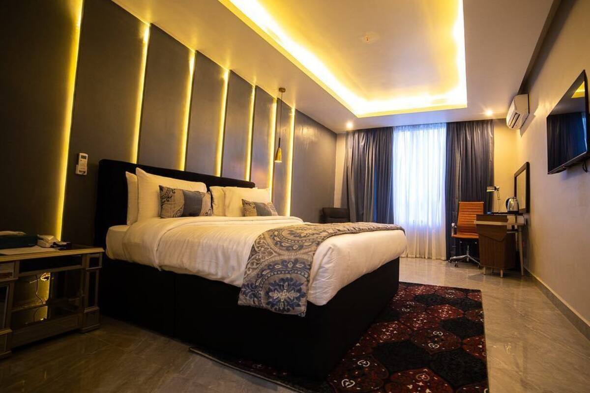 A modern hotel room with a large bed, bedside table, and a flat-screen TV mounted on the wall.
