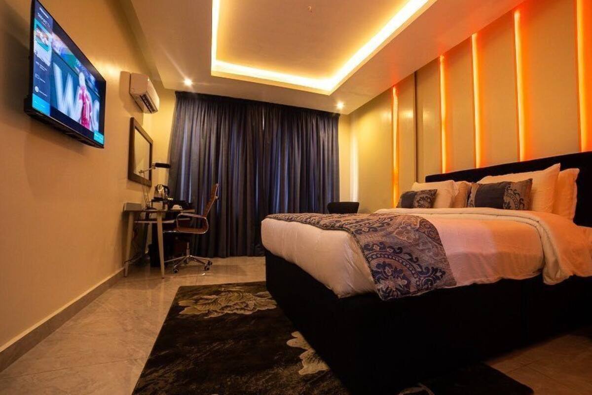 A modern hotel room with a large bed, a desk, a television, and a dark curtain.