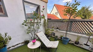 Un pequeño patio con césped artificial, una silla de lounge a rayas y plantas en macetas.