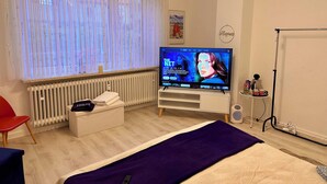 Una habitación de hotel moderna con una televisión grande, un radiador, una silla roja y una cama con una manta morada.
