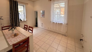 Una habitación amplia con una mesa y sillas para comer, una ventana con cortina, y un radiador en la pared.