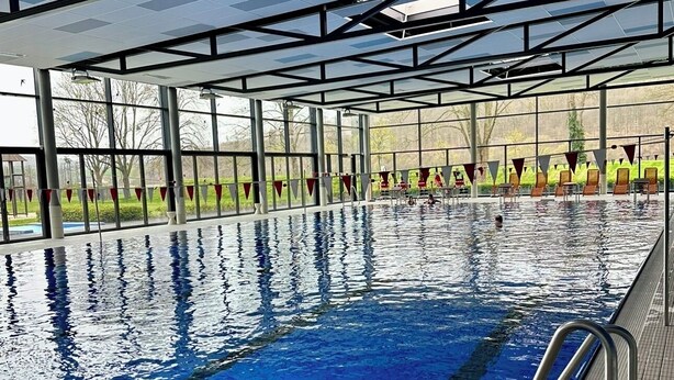 Una piscina interior con agua cristalina y azul, rodeada de amplios ventanales y barandillas de metal.