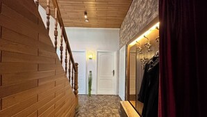 Un pasillo con una escalera de madera, una alfombra estampada, una puerta con una lámpara y un espejo con ropa colgada.