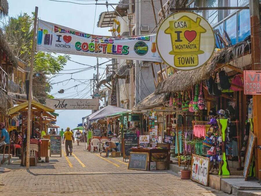 Un marché de rue animé, avec de nombreux étals et enseignes, dont l’une indique : « J’adore Montanita. »