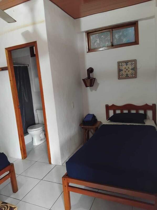 A bedroom with a bed, a small table, a wall-mounted lamp, and a window with a decorative frame. - Hotel SoleMare (Manglaralto)