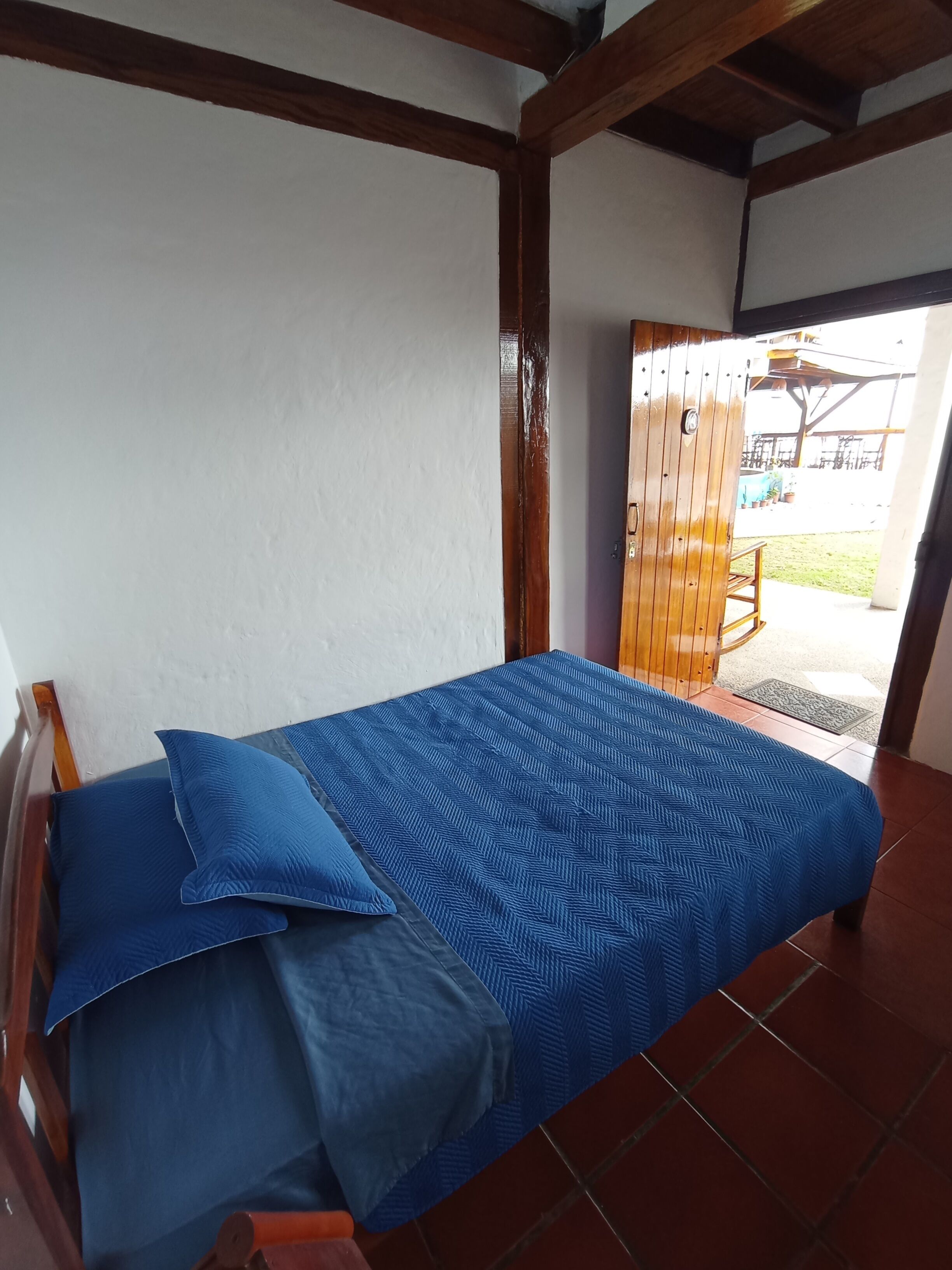Una cama con ropa de cama azul en una habitación con paredes blancas y vigas de madera.