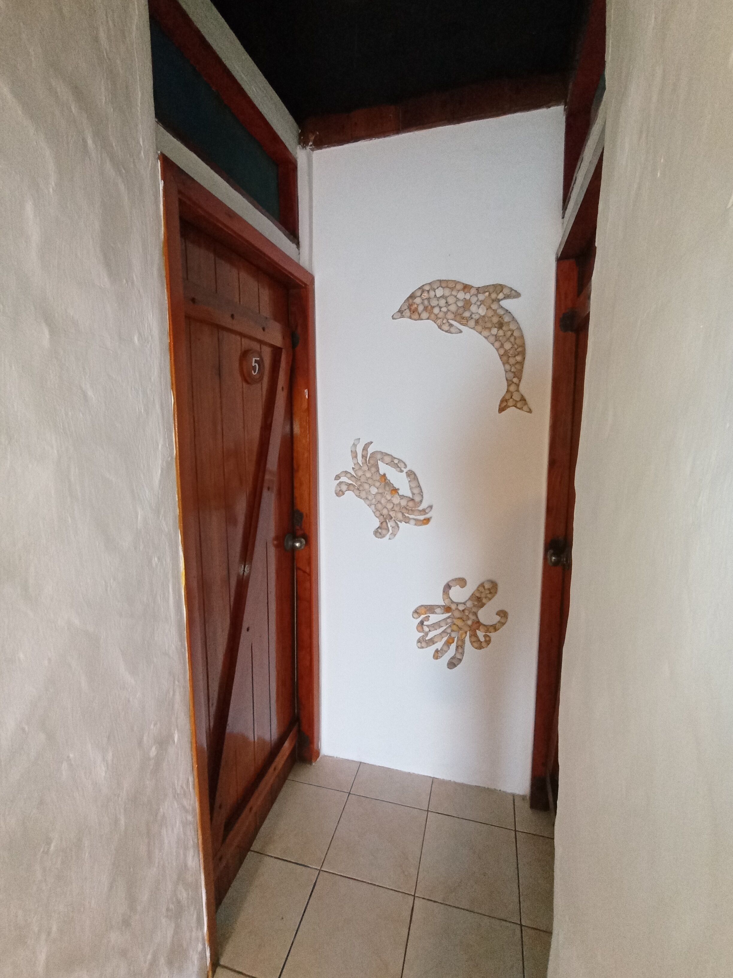 A hallway with a wooden door marked with the number 5, a tiled floor, and a wall with a dolphin and octopus mural.