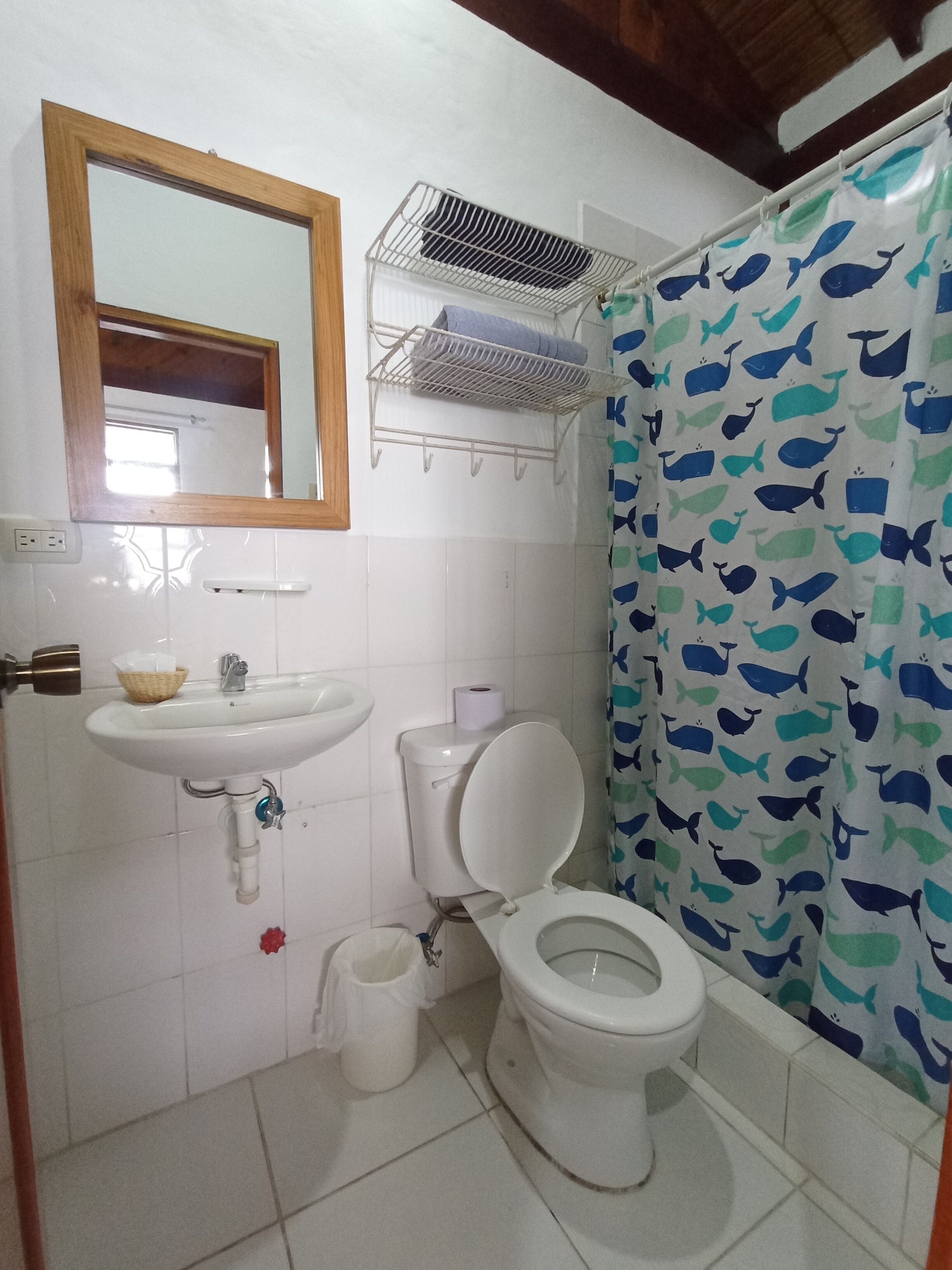 A bathroom with a white sink, toilet, and shower curtain with a whale pattern.