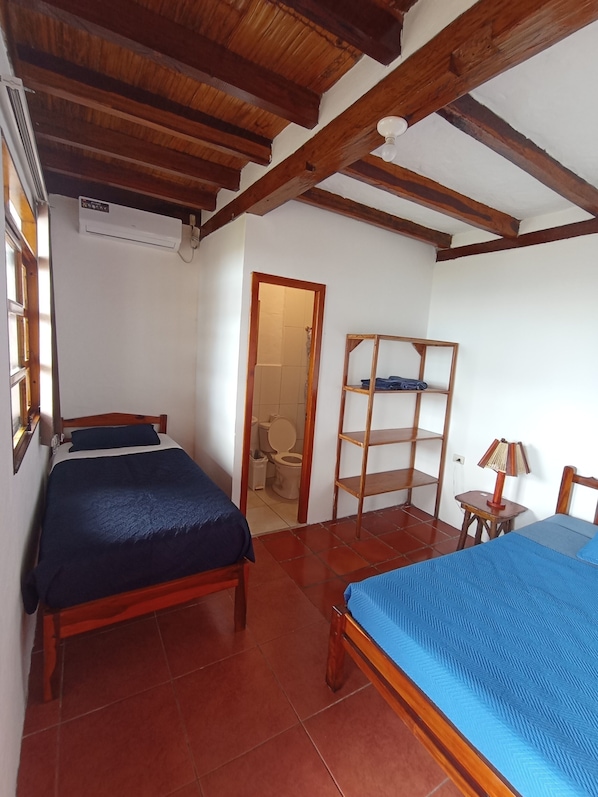A bedroom with two beds, a wooden ceiling, a small table with a lamp, and a wooden shelf unit. - Hotel SoleMare (Manglaralto)