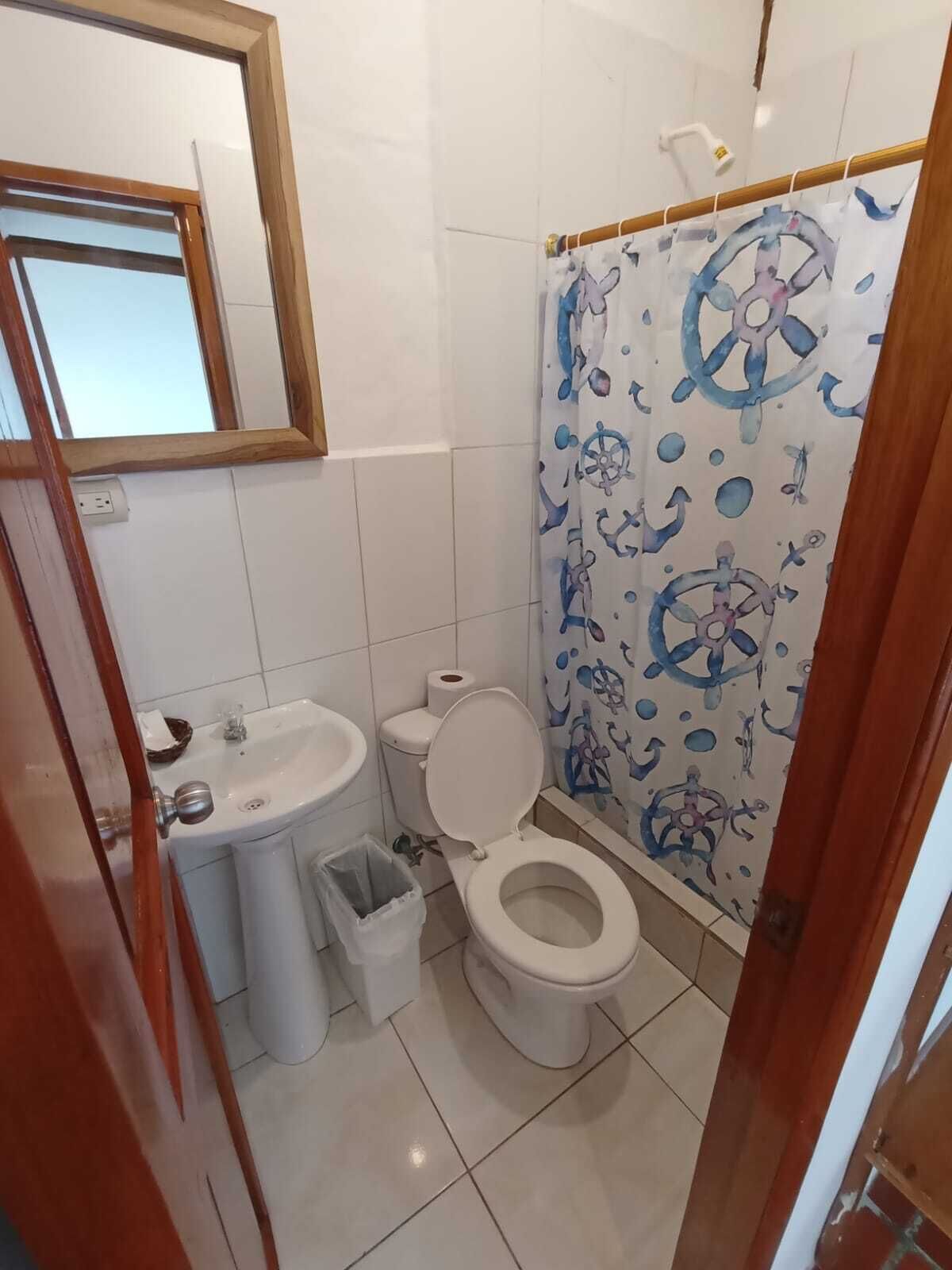 A small bathroom with a toilet, sink, and a shower curtain with nautical designs.
