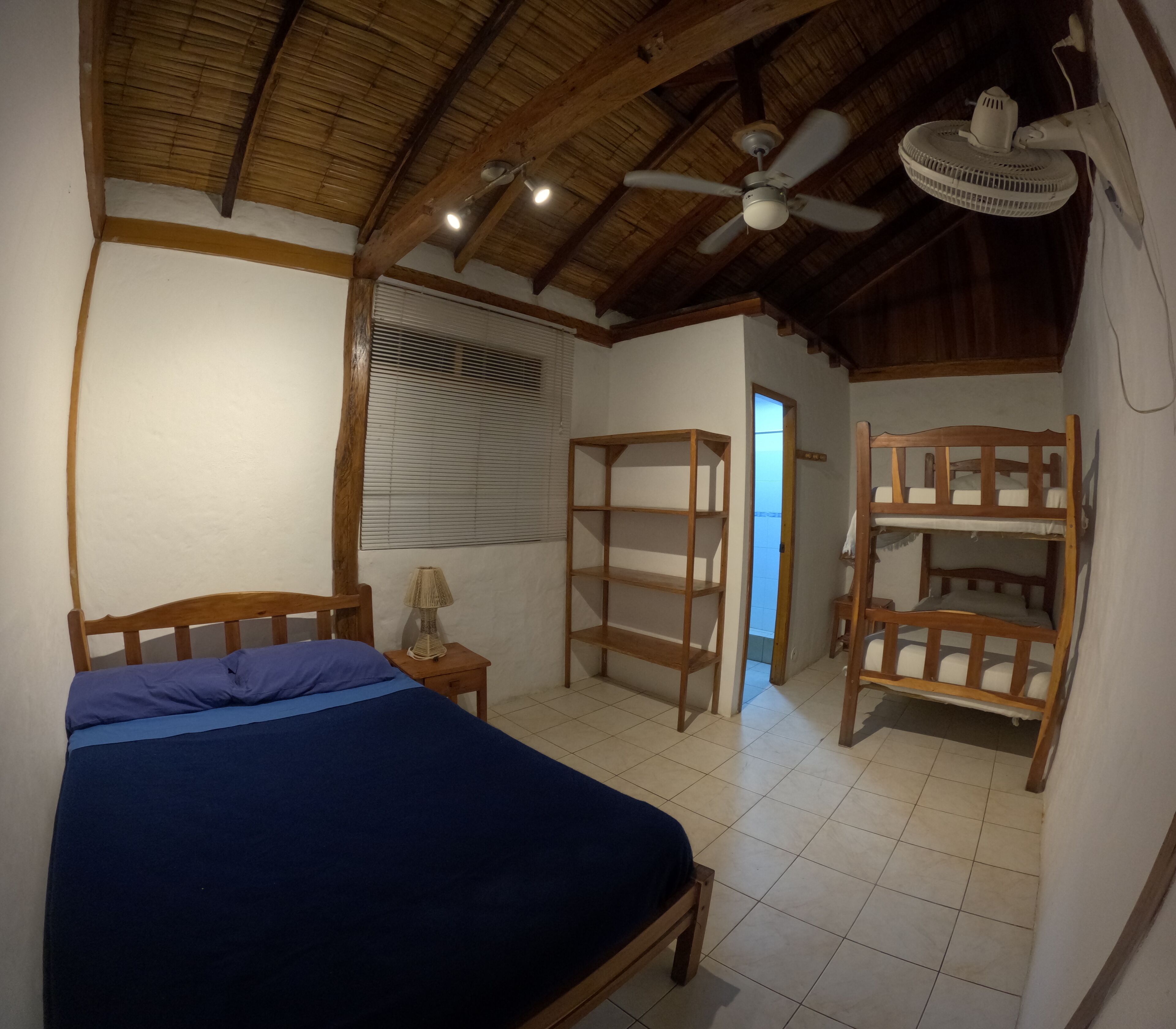 A room with a bed, a ceiling fan, a window with blinds, and a wooden bunk bed.