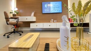 A modern hotel room with a wooden desk, a comfortable chair, a TV mounted on the wall, and a decorative vase with a bottle. - Rustic charm meets modern elegance at our wood & white retreat. (Butuan City)