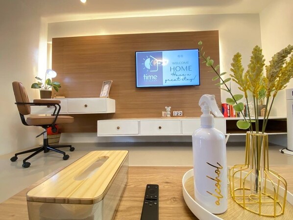 A modern hotel room with a wooden desk, a comfortable chair, a TV mounted on the wall, and a decorative vase with a bottle. - Rustic charm meets modern elegance at our wood & white retreat. (Butuan City)