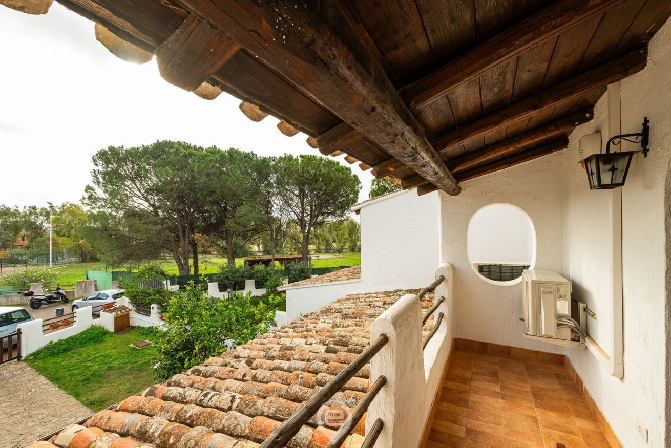 A balcony with a tiled floor, a wooden railing, and a view of a garden with trees and parked cars.
