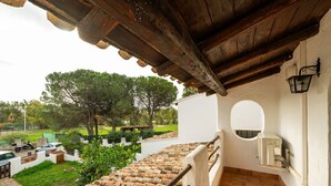 Un balcon doté d’un sol carrelé, d’une balustrade en bois et offrant une vue sur un jardin avec des arbres et des voitures garées.