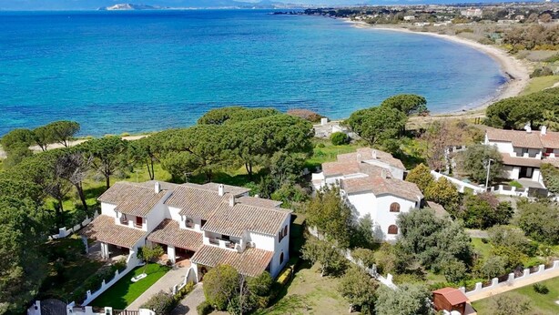 Vue aérienne d’une zone résidentielle côtière, avec des maisons, une plage et une mer bleue et limpide.