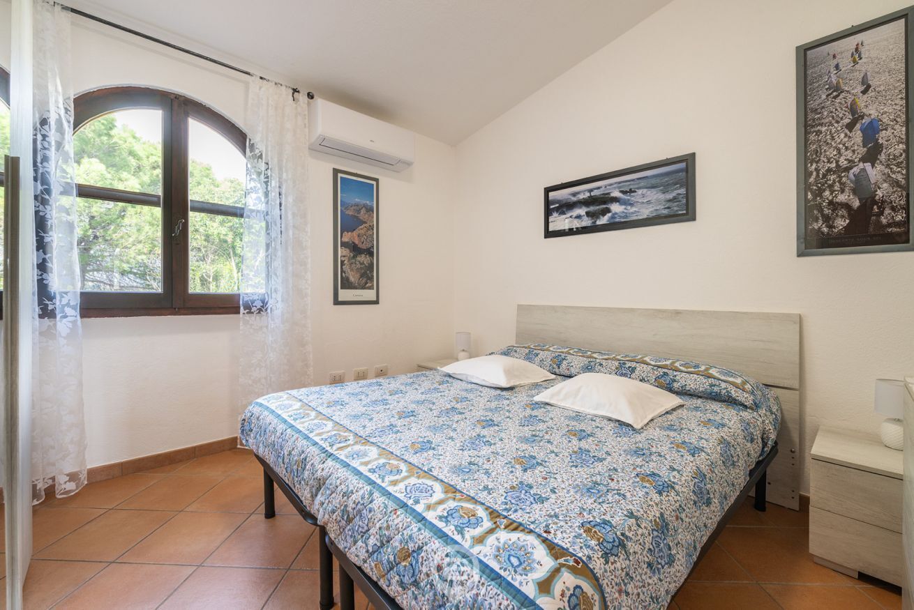 Un dormitori amb un llit, una finestra amb cortines, aire condicionat fixat a la paret i quadres emmarcats.