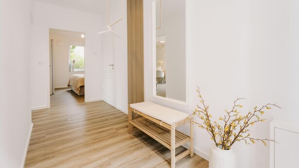 A hallway with a wooden bench, a large mirror, and a white vase with branches.