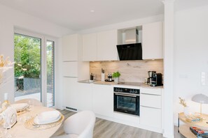 Una cocina moderna con armarios blancos, horno integrado y un comedor con una mesa lista para dos personas.