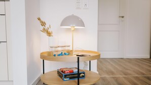 A two-tiered wooden side table with a lamp, a vase with dried plants, and a box of books.