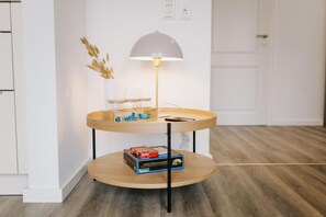 A two-tiered wooden side table with a lamp, a vase with dried plants, and a box of books. - de See - Suite 3 Seitliche Deichlage (Greetsiel)