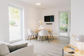 A modern living room with a dining area, a flat-screen TV mounted on the wall, and large windows. - de See - Suite 3 Seitliche Deichlage (Greetsiel)