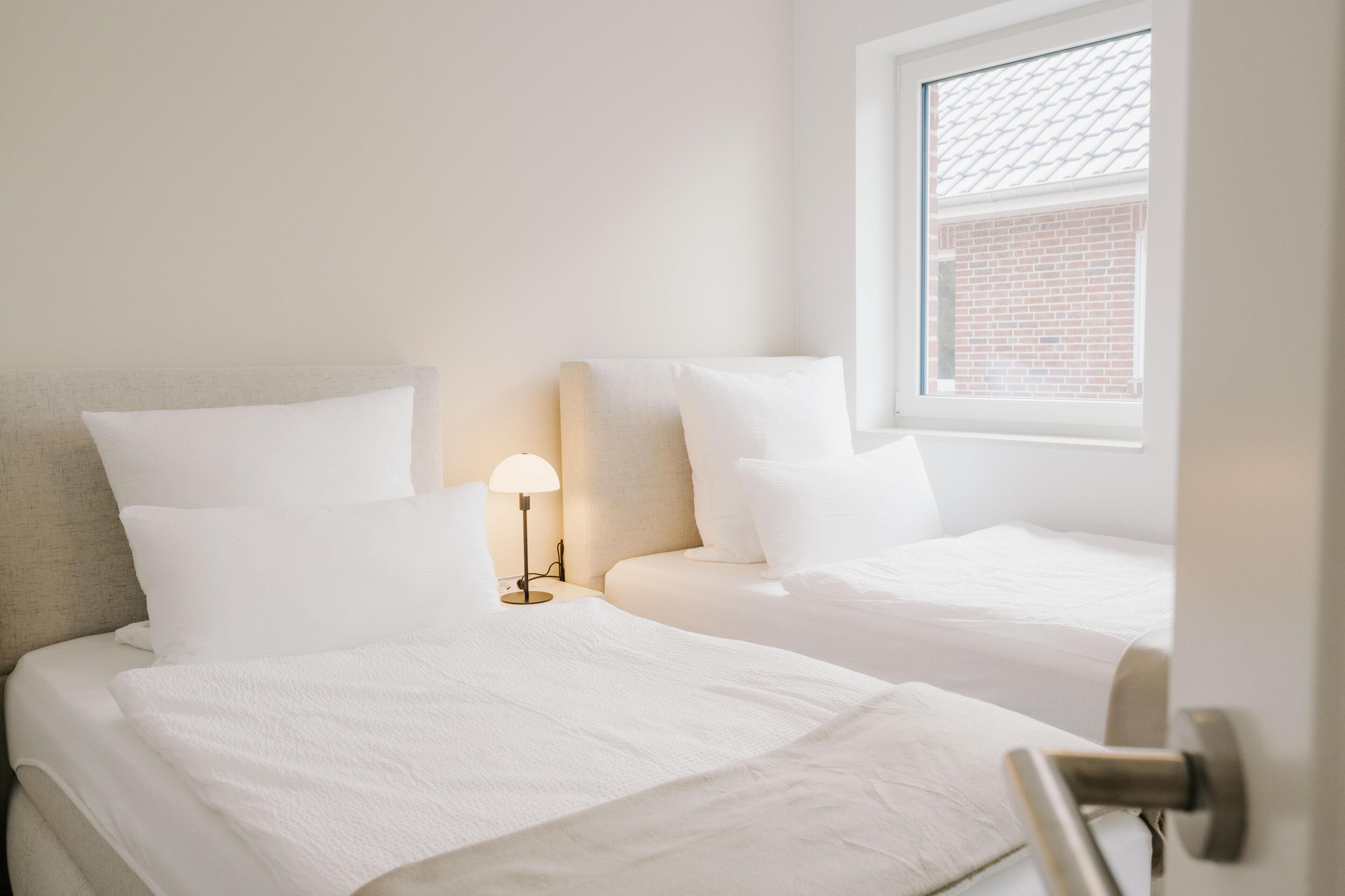 A hotel room with two beds, a nightstand with a lamp, and a window with a view of a brick wall.
