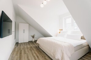 Une chambre avec un plafond en pente, un lit, une armoire et une fenêtre.
