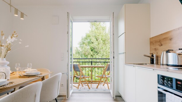A modern kitchen with a dining area, a view of the outdoors, and a built-in oven. - de See - Suite 4 Seitliche Deichlage (Greetsiel)