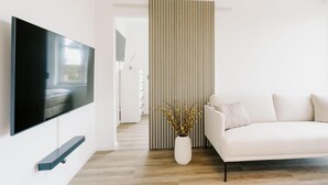 A modern living room with a flat-screen TV, a white sofa, a decorative vase, and a striped partition. - de See - Suite 4 Seitliche Deichlage (Greetsiel)