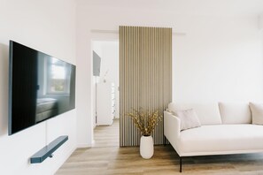 Ett modernt vardagsrum med en platt-TV, en vit soffa, en dekorativ vas och en randig rumsavdelare.
