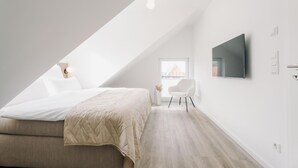 A modern bedroom with a bed, a TV, a chair, and a window. - de See - Suite 4 Seitliche Deichlage (Greetsiel)